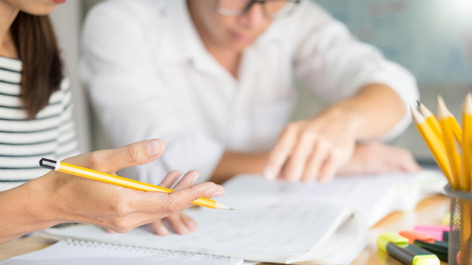 A person holding a pencil while looking at a sheet of paper