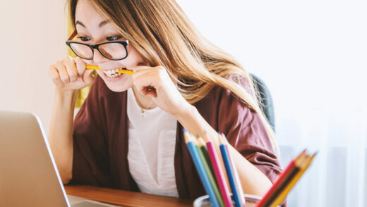 A person biting a pencil while looking at a computer